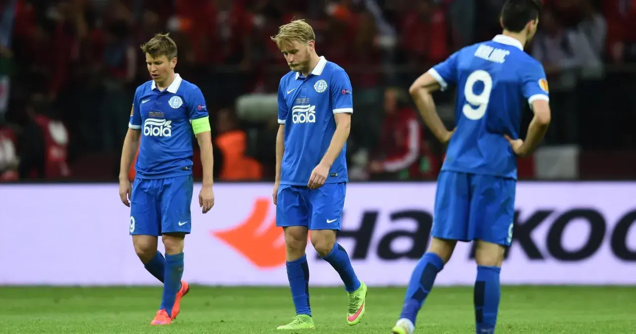 Smutni piłkarze Dnipro Dniepropietrowsk w niebieskich strojach schodzą z boiska po przegranym meczu.