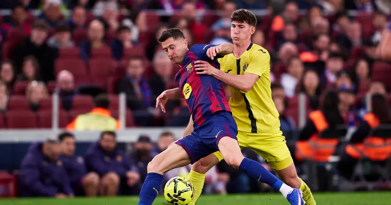 Piłkarz Barcelony Robert Lewandowski w akcji, walczy o piłkę z obrońcą. Kibice na trybunach obserwują mecz, martwiąc się o lewandowski kontuzja.