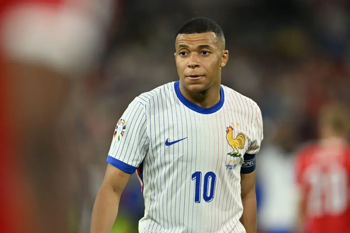 Kylian Mbappé w białej koszulce z numerem 10 i symbolem koguta, reprezentujący Francję. Jego obecne drużyny to PSG i reprezentacja Francji.