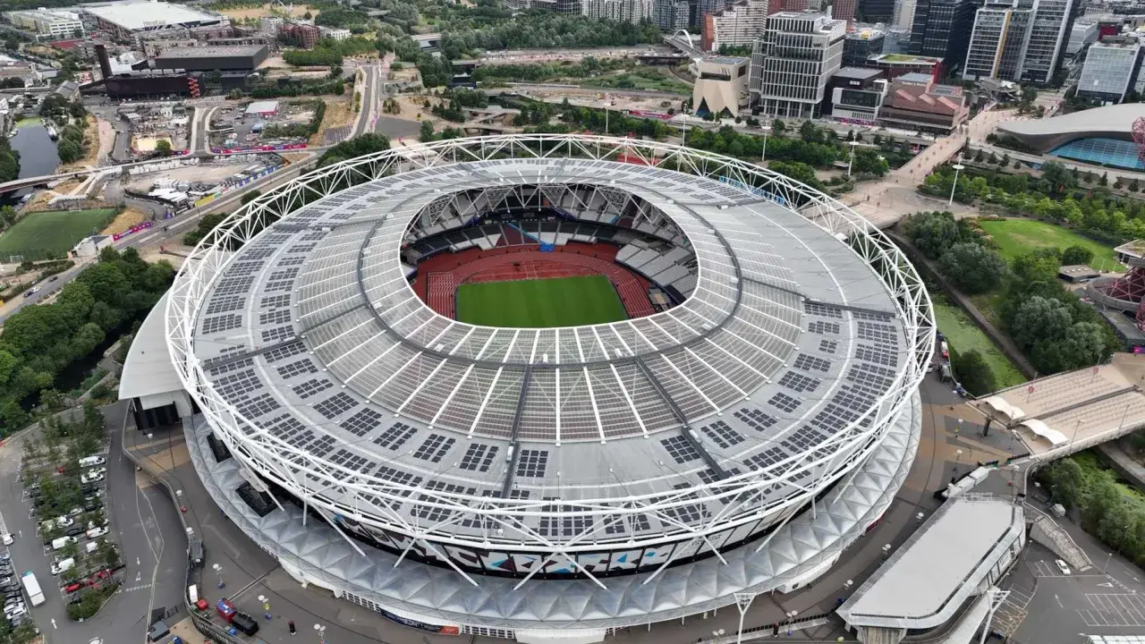 Widok z lotu ptaka na londyński stadion z zieloną murawą i bieżnią. Dach pokryty panelami słonecznymi.