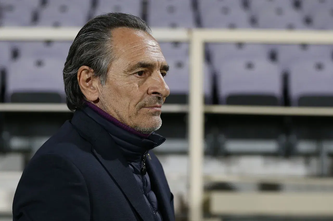 Prandelli, zamyślony trener, w ciemnej kurtce i marynarce, z fioletowym kołnierzem, na tle pustych trybun.