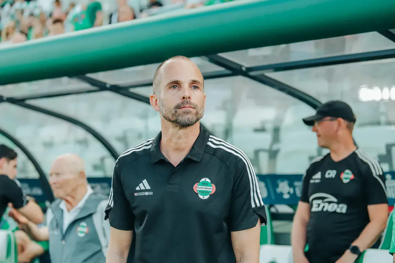 Trener Radomiaka w czarnej koszulce z herbem klubu, skupiony na boisku.