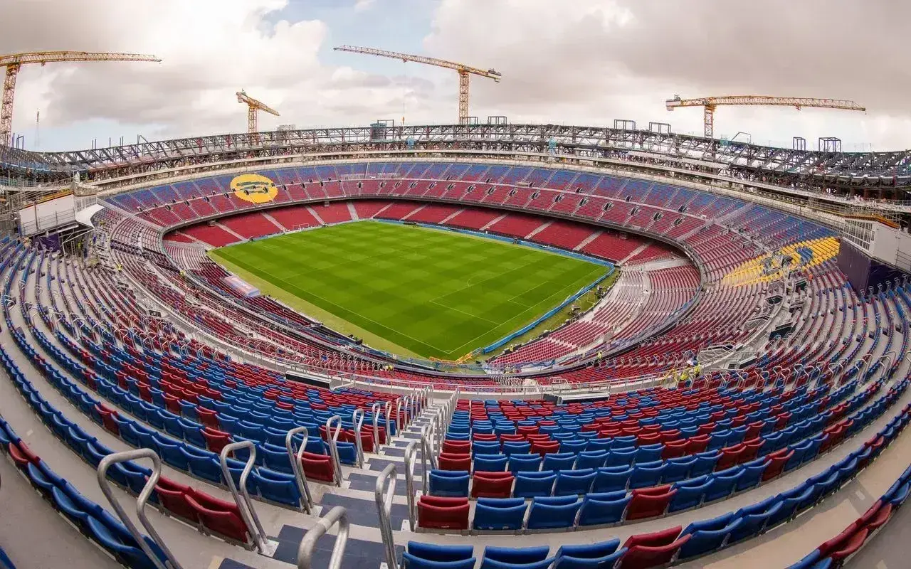 Widok na pusty stadion z czerwono-niebieskimi trybunami, zieloną murawą i dźwigami w tle. To z pewnością najładniejszy stadion w Polsce, czekający na kibiców.