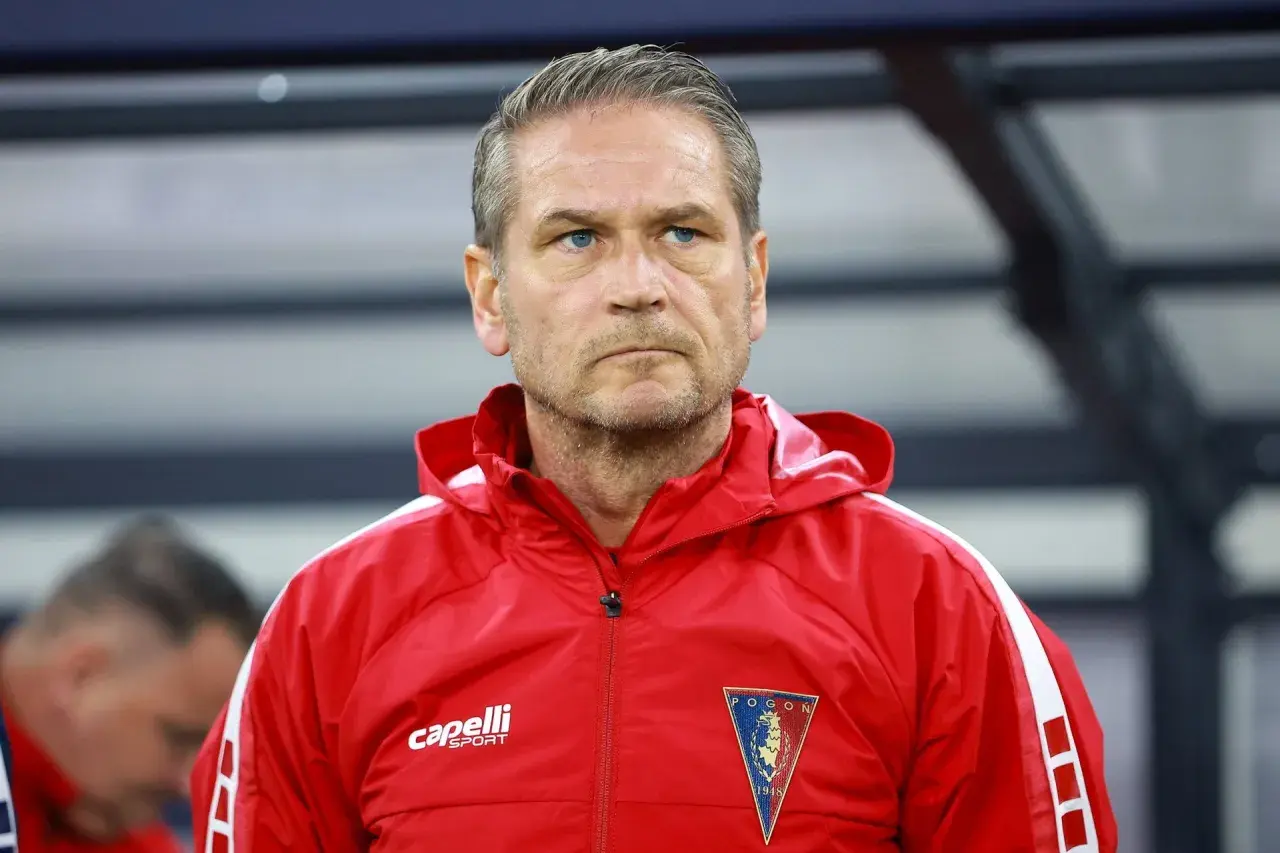 Twarz trenera Pogoni Szczecin, zamyślony, w czerwonej kurtce sportowej z herbem klubu.