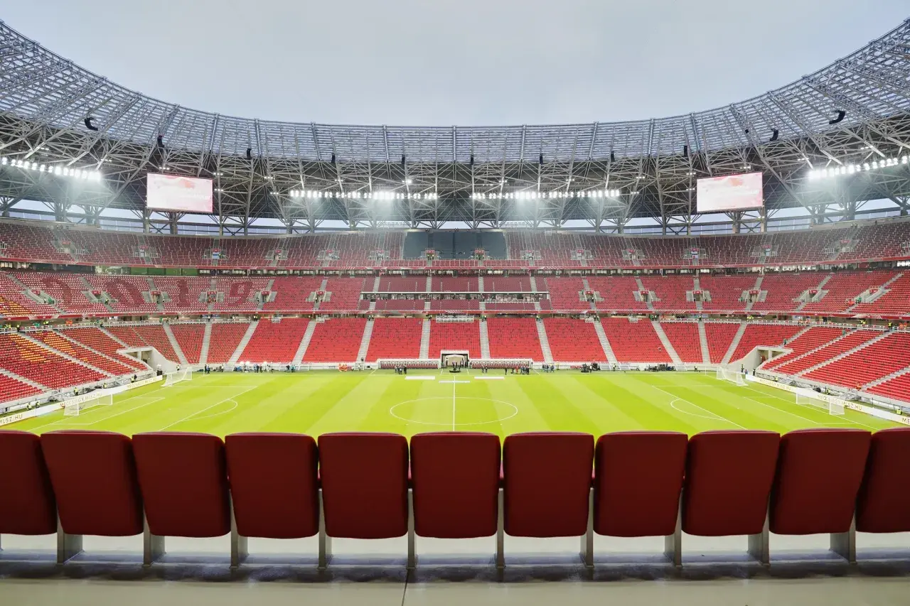 Pusta, nowoczesna arena sportowa w Budapeszcie, z rzędami czerwonych siedzeń i zieloną murawą.