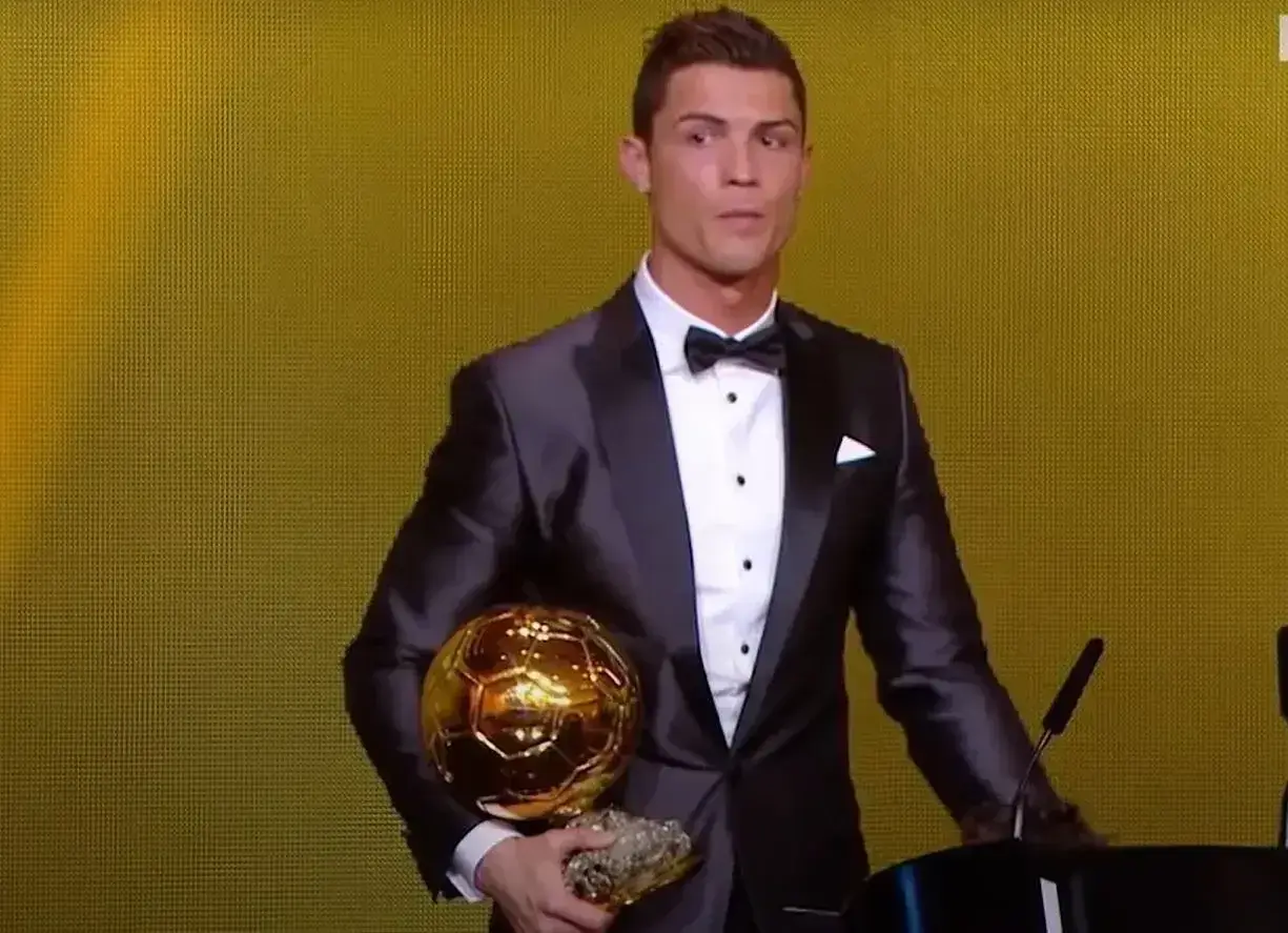 Cristiano Ronaldo w garniturze trzyma złotą piłkę. Ile złotych piłek ma Ronaldo? To pytanie zadaje sobie wielu fanów.