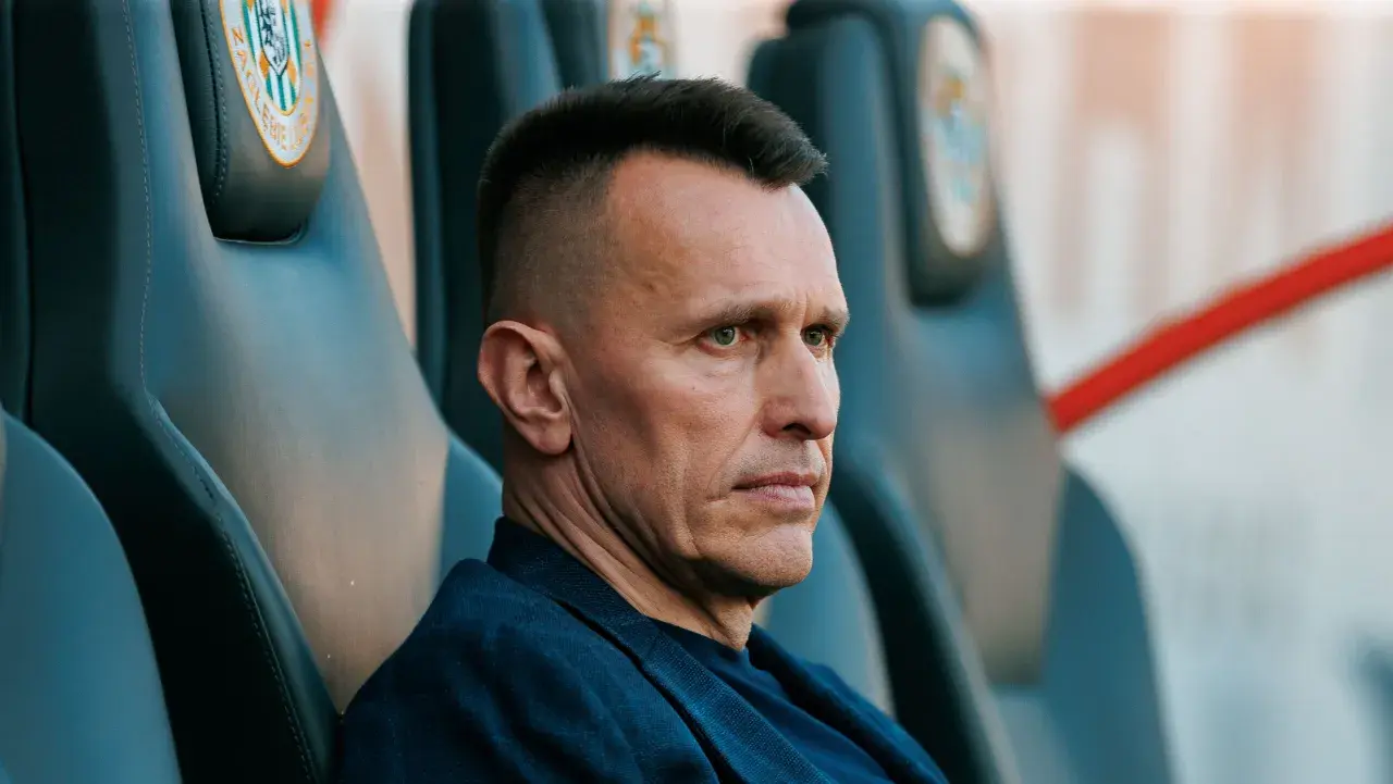 Skupiony trener Zagłębia Lubin siedzi na ławce rezerwowych, analizując grę.