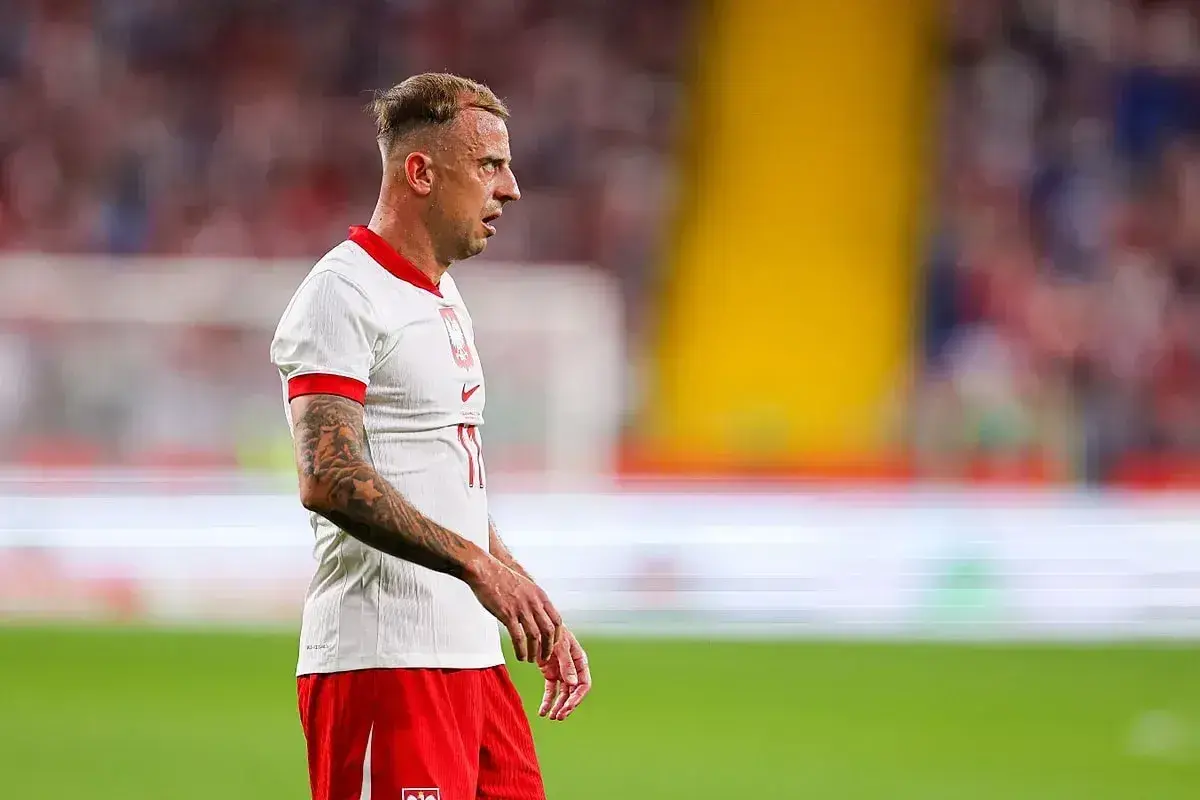 Piłkarz Kamil Grosicki w białej koszulce i czerwonych spodenkach, z tatuażami na ramieniu. Jego majątek to wynik ciężkiej pracy na boisku.