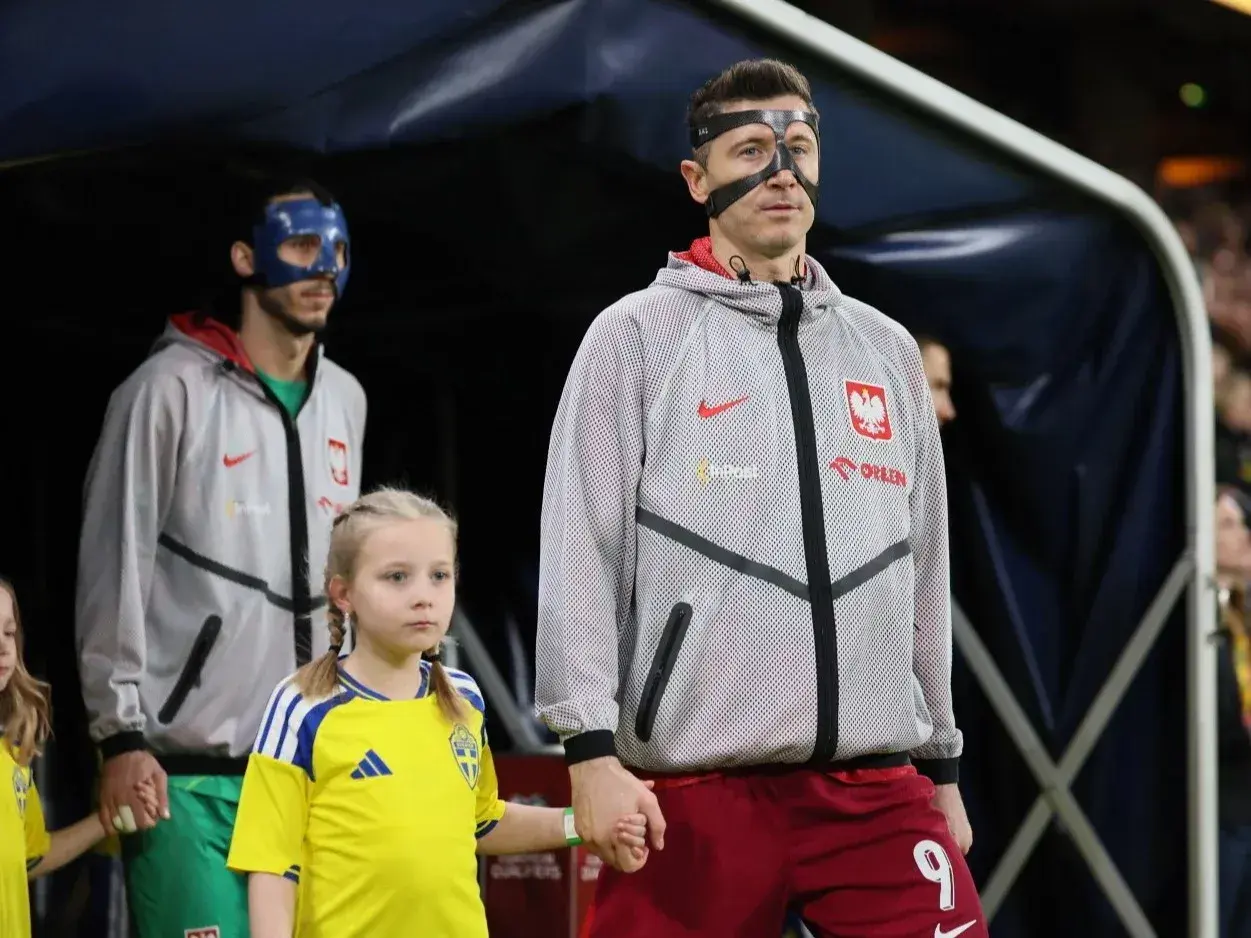Polscy piłkarze, w tym Robert Lewandowski, wychodzą na murawę z dziećmi. Jeden z zawodników ma niebieską maskę.