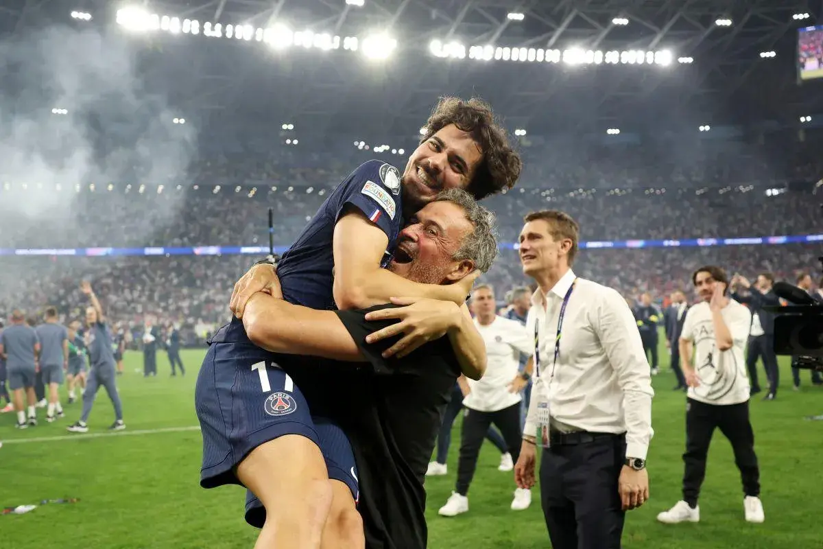 Radość piłkarza PSG obejmującego trenera. W tle tłum kibiców i stadion.