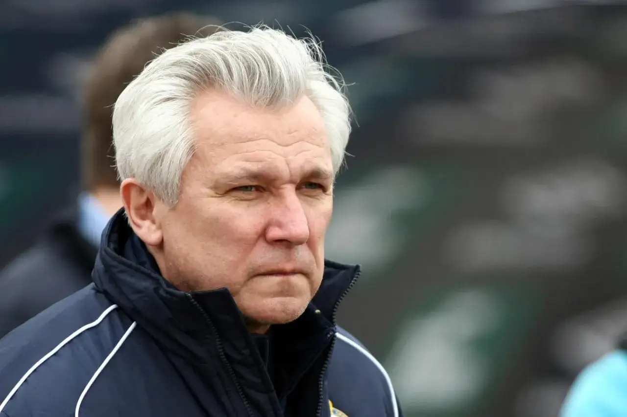 Portret Henryka Kasperczaka, trenera z siwymi włosami, w ciemnej kurtce sportowej.