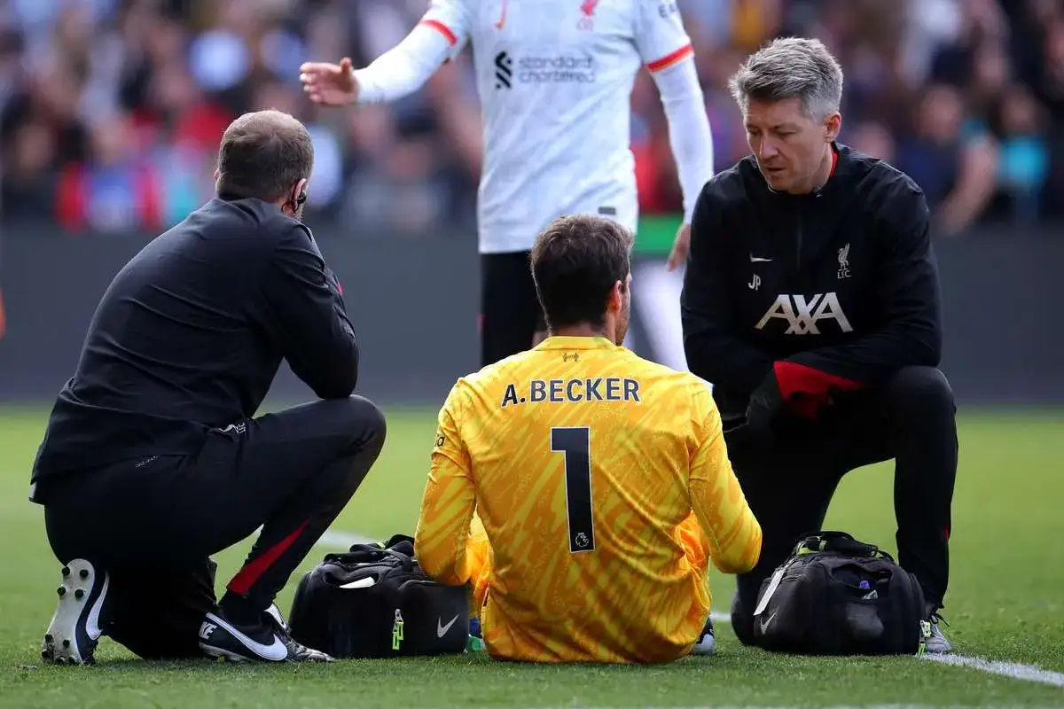 Bramkarz Liverpoolu, Alisson Becker, siedzi na murawie otoczony przez sztab medyczny.