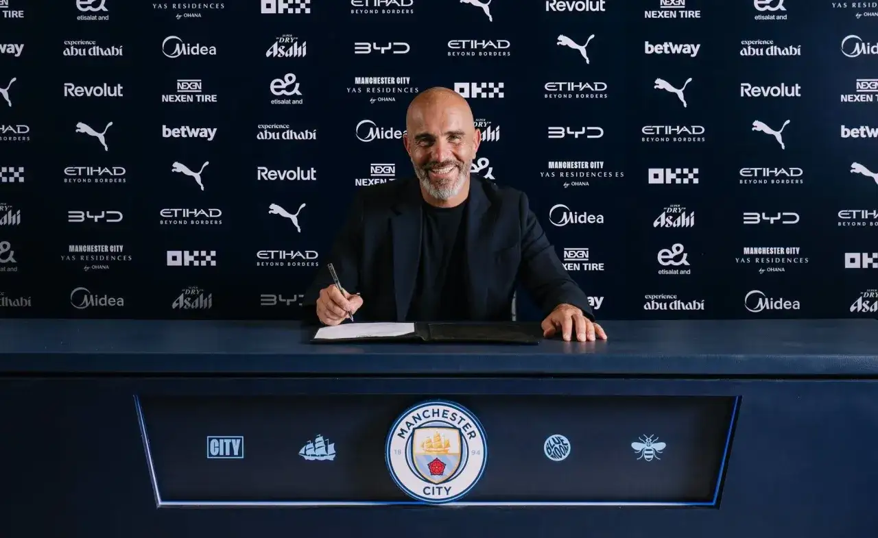 Uśmiechnięty trener Manchesteru City, podpisujący dokumenty.