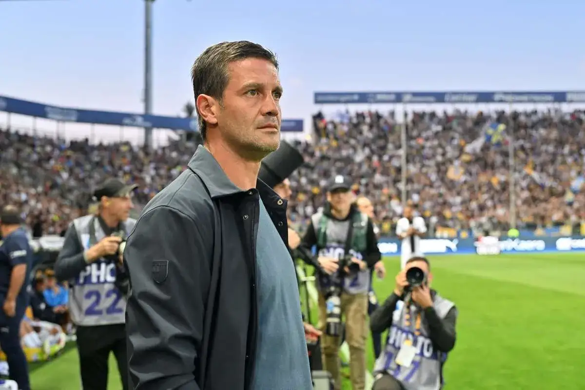 Mężczyzna w kurtce, prawdopodobnie inter trener, obserwuje mecz na pełnym stadionie.