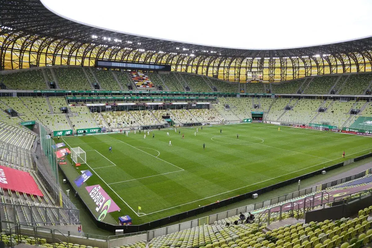 Stadion Lechii Gdańsk, z zielonymi trybunami i boiskiem, gotowy na mecz. Jego pojemność pozwala na przyjęcie tysięcy kibiców.