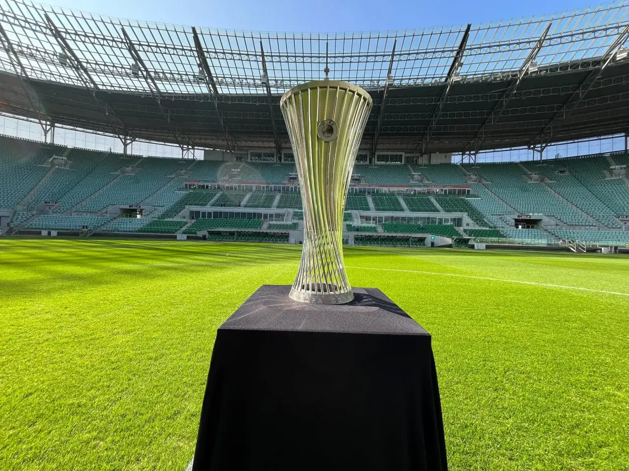 Trofeum Ligi Konferencji Europy UEFA błyszczy na tle pustego stadionu.