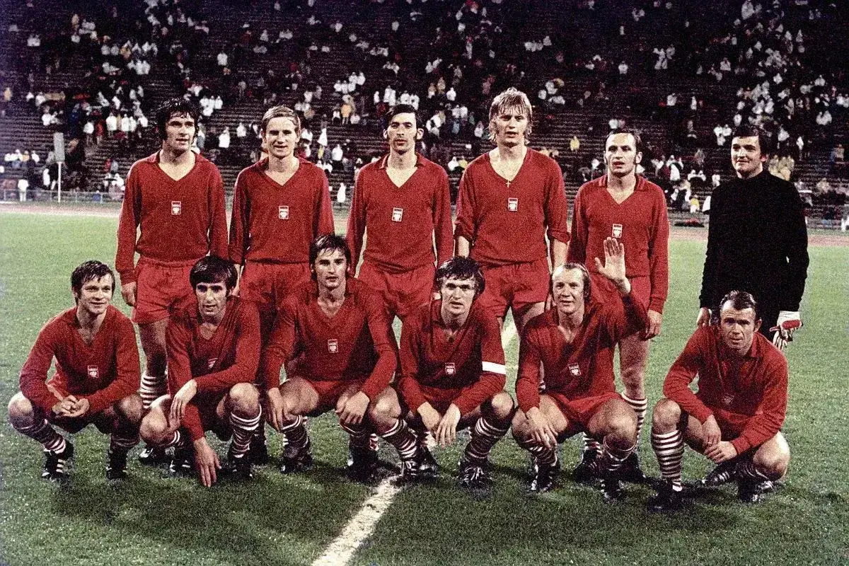 Byli piłkarze reprezentacji Polski w czerwonych strojach pozują na boisku.