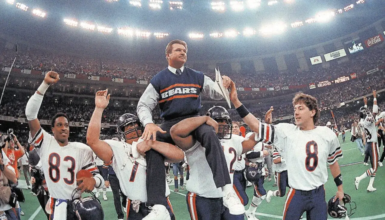 Sławni piłkarze Chicago Bears świętują zwycięstwo, niosąc trenera na ramionach. Stadion wypełniony kibicami.