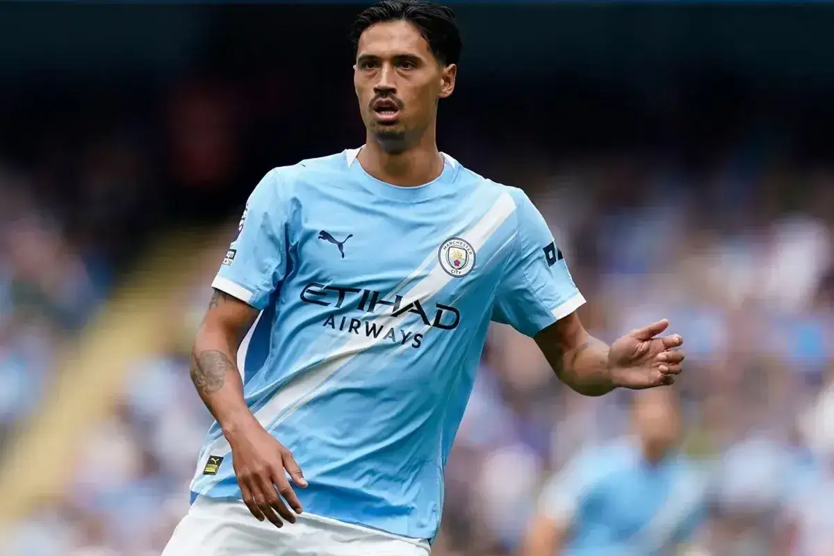 Piłkarze Manchesteru City w błękitnych strojach, jeden z nich, z tatuażem na ramieniu, skupiony na grze.