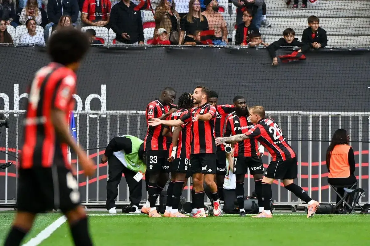 Piłkarze OGC Nice świętują bramkę. Zawodnicy w czarno-czerwonych strojach cieszą się razem na boisku, otoczeni przez kibiców na trybunach.