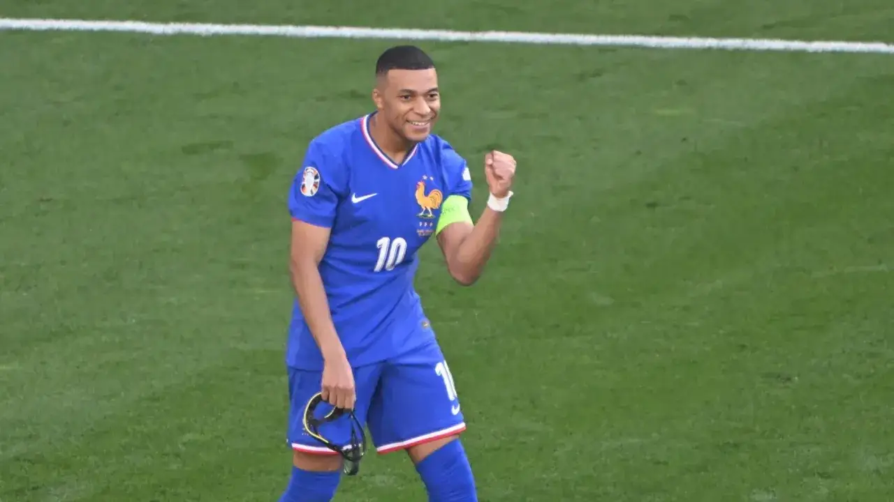 Kylian Mbappé w niebieskiej koszulce reprezentacji Francji, z numerem 10, świętuje na boisku. Jego obecne drużyny to Francja i PSG.