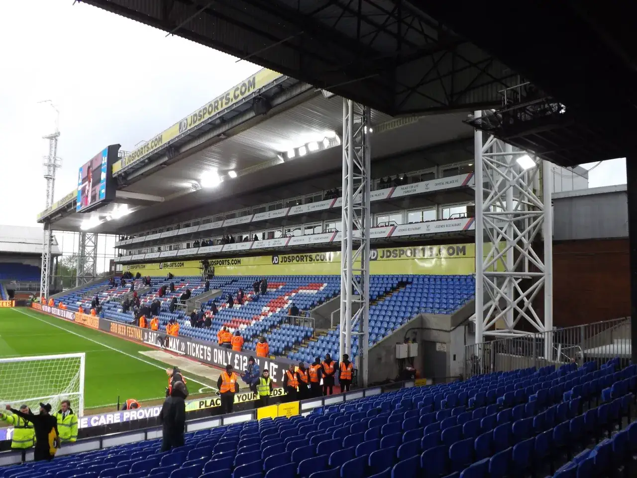 Trybuna stadionu Selhurst Park z niebieskimi i czerwonymi siedzeniami, zieloną murawą i tablicą wyników.