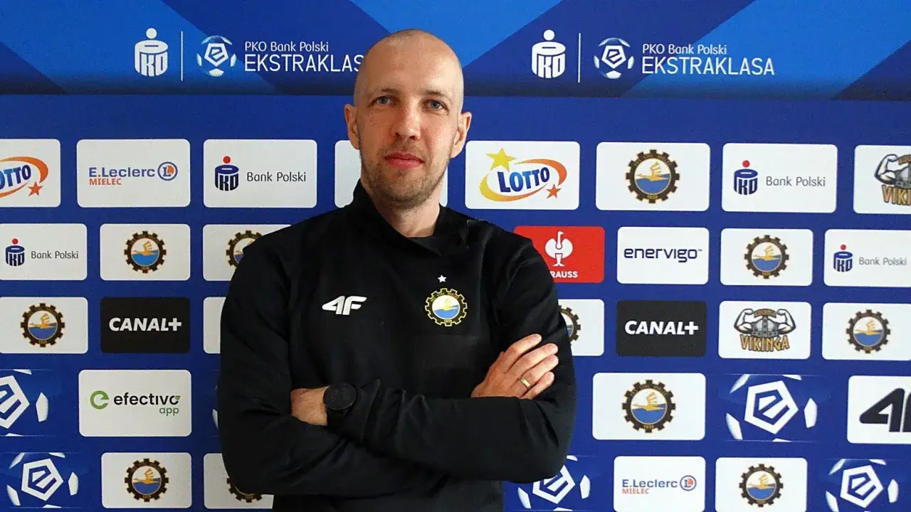 Trener Stali Mielec w czarnej bluzie z herbem klubu. Tło z logotypami sponsorów Ekstraklasy.
