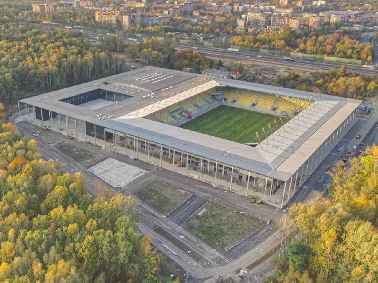 Nowoczesny stadion z żółtymi trybunami, otoczony jesiennym lasem. Wielu uważa go za najładniejszy stadion w Polsce.