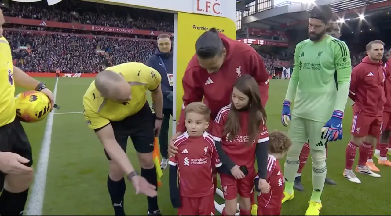 Dzieci w strojach Liverpoolu, w tym mały chłopiec, który wygląda jak Diego Jota, czekają na wyjście na boisko.